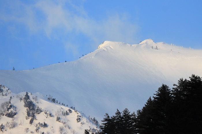国道３５２号線、高畑スキー場と小豆温泉間のほぼ中間地点より望む三ツ岩岳の厳寒の光景です。この地点より小豆温泉を通って４㎞区間が昔から中一里として、豪雪の最難関地点(中一里＝４㎞）と言われてきました。会津駒ケ岳と三ツ岩岳から吹き降ろす暴風雪も時にすさまじく、ホワイトアウトも頻繁に発生し、大雪の深夜には幾度となく多くの車が走れなくなって、スノーシェッド内に車中泊、などの歴史的な経緯もある大雪の区間です（２０２３年２月１８日）。